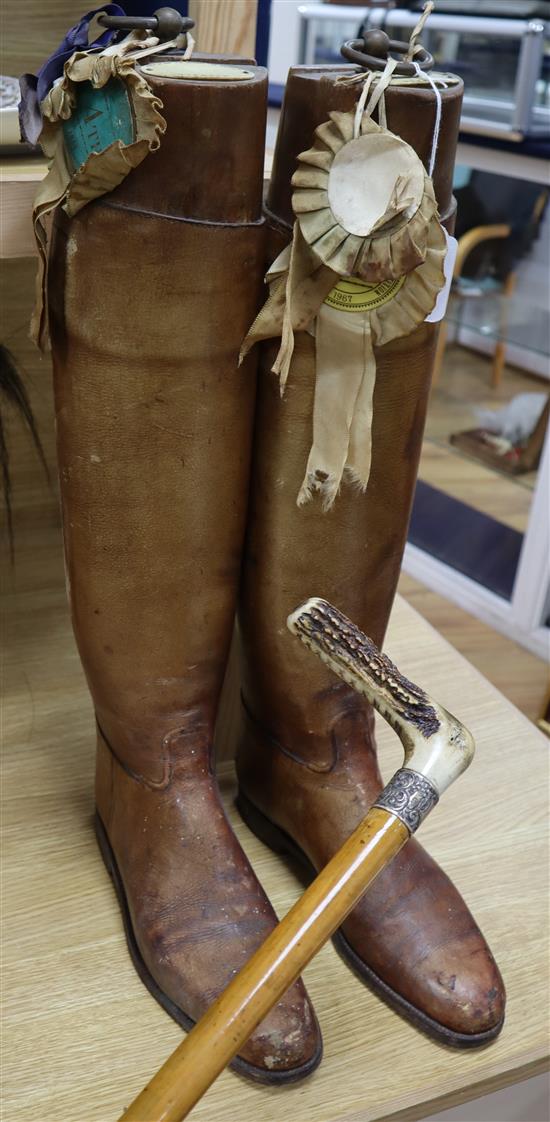 A pair of vintage riding boots with trees and a silver-collared cane riding stick